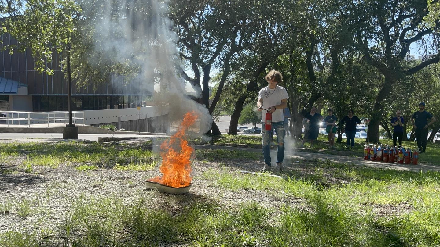 photo of student putting out a fire with a fire extinguisher