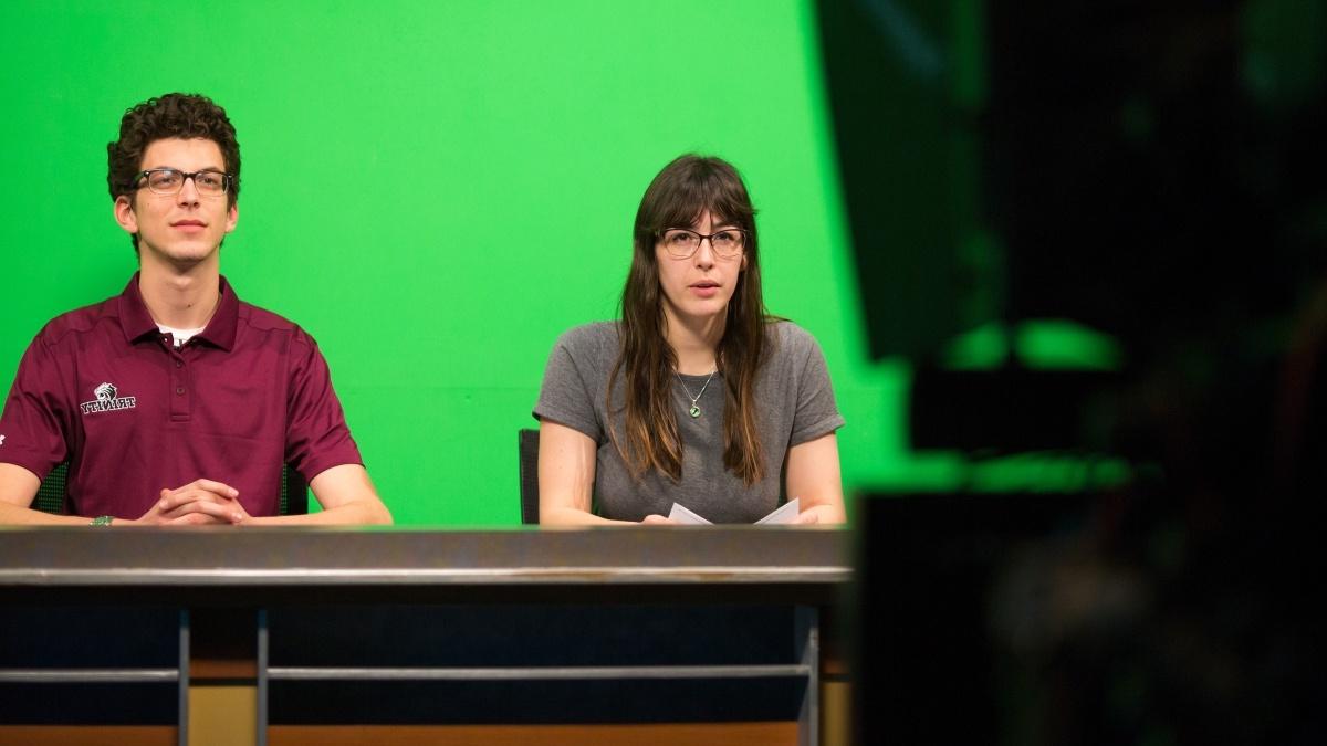 Students sitting in front of a teleprompter in front of the green screen
