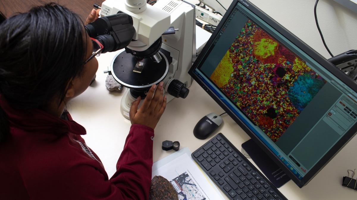 Woman looks at cells through a microscope.