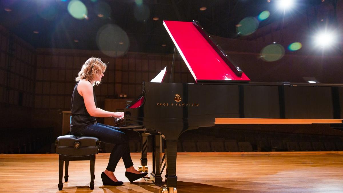student gives a piano performance on a lit stage