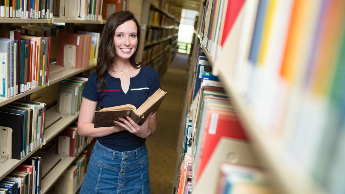 年轻女子拿着一本书，站在科茨图书馆的书架之间